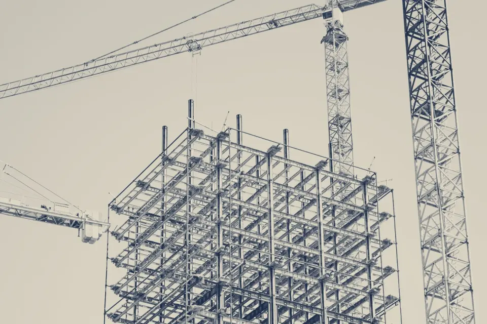 Estructura metálica de un edificio en construcción junto a una grúa torre, tratada en duotono azul marino